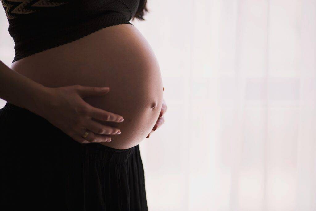 Profile shot of pregnant woman wearing a bra and skirt and holding her stomach