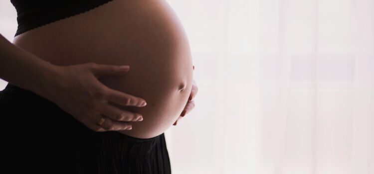 Profile shot of pregnant woman wearing a bra and skirt and holding her stomach