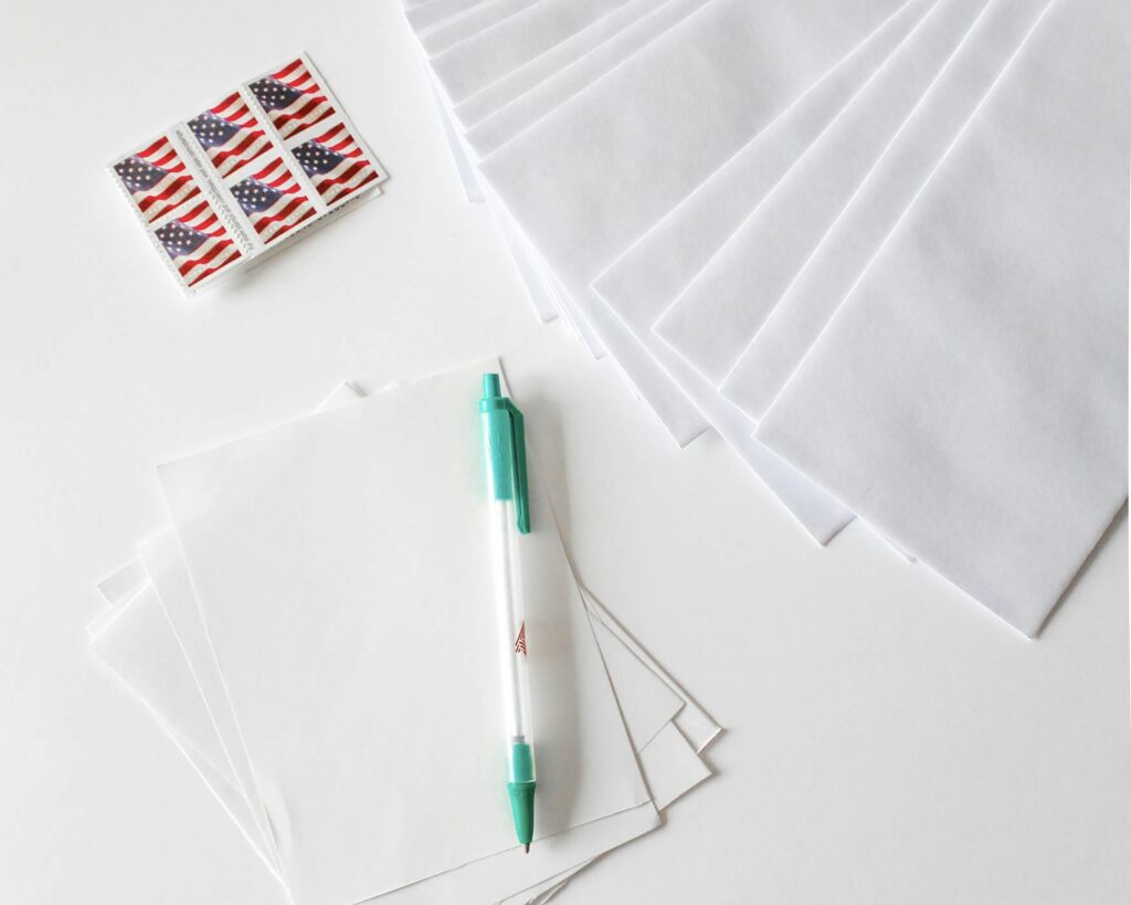 A series of American flag stamps, envelopes, white paper, and a pen on a table