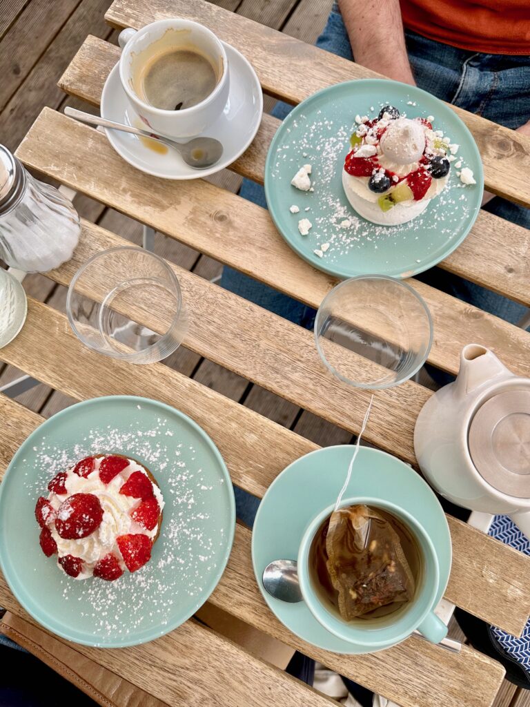 Two desserts featuring Chantilly whipped cream and fresh fruit, one cup of coffee, and one cup of tea on a table